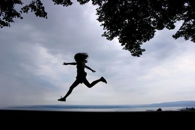 Side view of silhouette teenage girl jumping at beach against cloudy sky