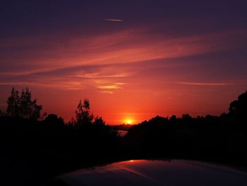 Silhouette trees on landscape against orange sky