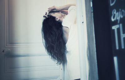 Side view of woman holding dry flowers while standing at doorway