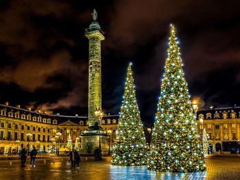 Illuminated christmas tree against building at night