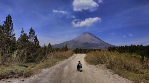 People riding motorcycle on road by mountain against sky