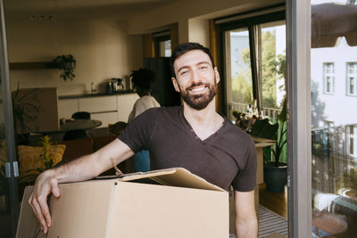 Portrait of smiling man carrying cardboard box at new home