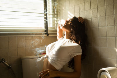 Young woman smoking cigarette in bathroom