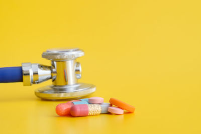 Close-up of medicines and stethoscope on yellow background