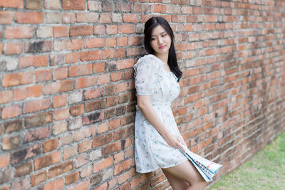 Portrait of beautiful young woman standing against brick wall