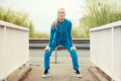 Full length portrait of young woman doing warm up exercises on footpath