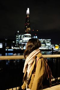 Rear view of woman against illuminated buildings in city at night