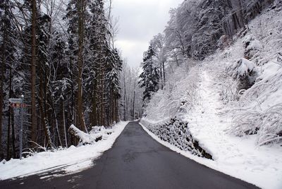 Snow covered road amidst trees against sky