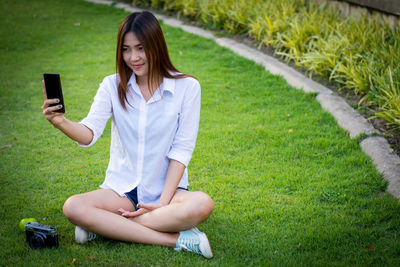 Young woman using phone while sitting on grass