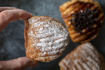 Two fingers of a female hand hold a sweet crescent with powdered sugar.