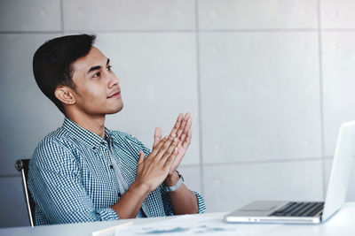 Young man looking away while sitting on wall