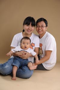 Portrait of smiling family sitting against colored background