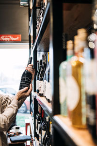 Customer selecting wine bottle from store shelf. a person's hand picking a wine bottle from 