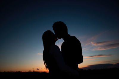 Young lovely couple hugging each other and kissing at orange sunset. silhouette at sunset background