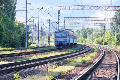 The outgoing old train rides along the railroad against the backdrop of city buildings in a haze