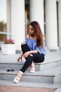 Young woman sitting on staircase against building