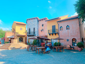 Chairs and tables at sidewalk cafe against blue sky