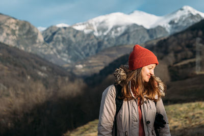 Smiling traveler at the snowy mountains. happy woman in red cap warming up and enjoying the sunlight