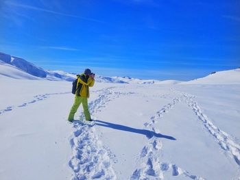 Man photographing on snowy land against blue sky