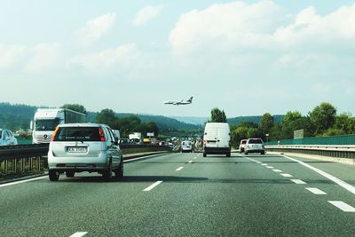 Airplane flying over road against sky
