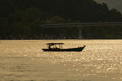 Silhouette boat sailing on river against sky