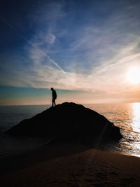 Silhouette man standing on beach against sky during sunset