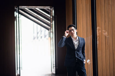 Portrait of confident young businessman standing by window at office