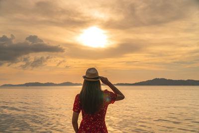 Rear view of woman standing by sea against sky during sunset
