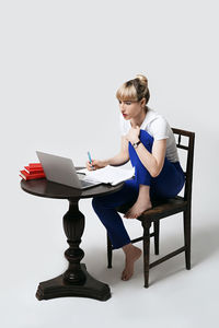 Portrait of young woman using laptop while sitting on chair against white background