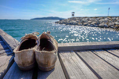 Close-up of shoes on pier over sea against sky