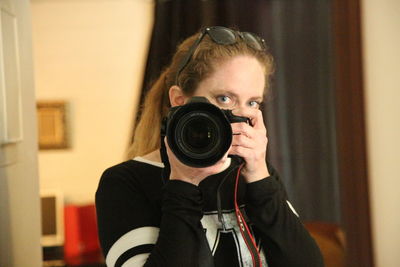 Portrait of woman holding camera reflecting on mirror at home