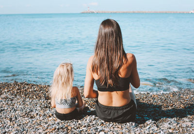 Rear view of mother and daughter sitting at beach