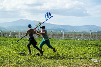 Refugees with greek flag running on grassy field