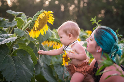 Mother carrying daughter by yellow flowering plants