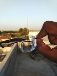 Close-up of hand holding eyeglasses against sky