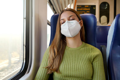 Relaxed beautiful woman with medical face mask sleeping sitting in the train. 