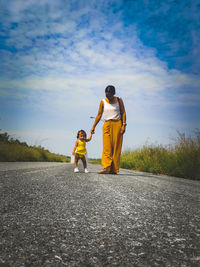 Rear view of mother and daughter standing on riverbank against sky