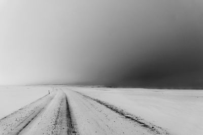 Empty road amidst snow covered field against clear sky during winter
