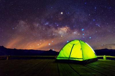 Glowing green camping tent on bamboo terrace under the night sky full of stars and the milky way, 
