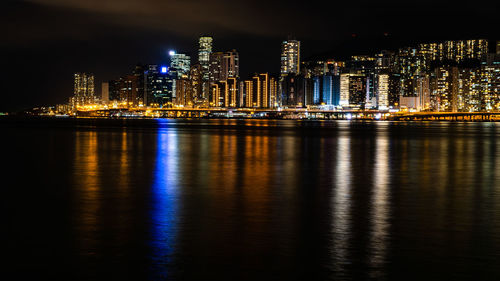 Illuminated buildings by river against sky at night