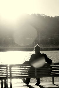 Rear view of man sitting by lake against sky