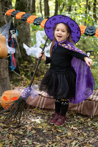 Happy girl in halloween costume and witch hat with broom in halloween decoration outdoor