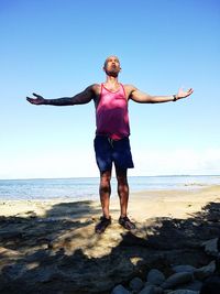 Full length of man with arms outstretched standing on beach against sky