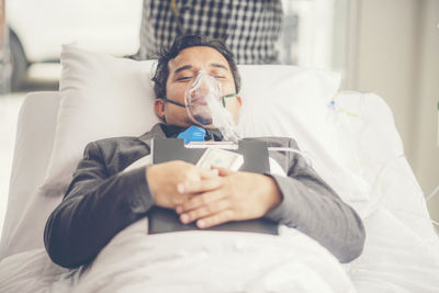 High angle view of patient with file and currency lying on bed in hospital