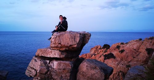 Man sitting on rock by sea against sky