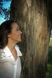 Young woman looking away against tree trunk