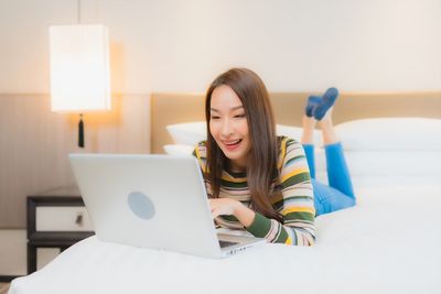 Portrait of smiling woman using phone while sitting on bed