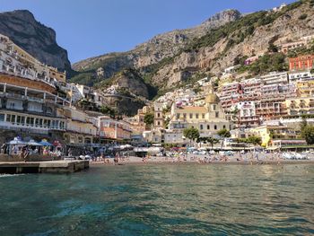 People on sea by mountain against clear sky