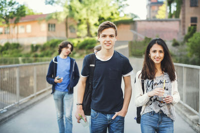 Portrait of smiling teenagers walking on bridge