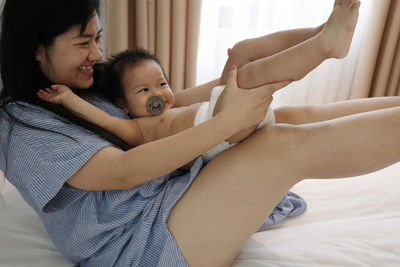 Mom is playing with a baby under 2 years old on a white-sheeted bed